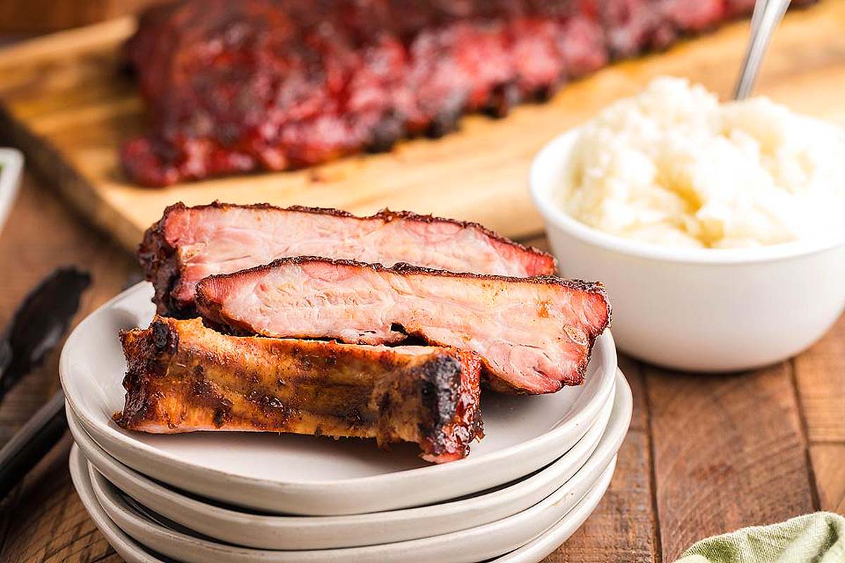 Smoked ribs stacked on a white plate. 