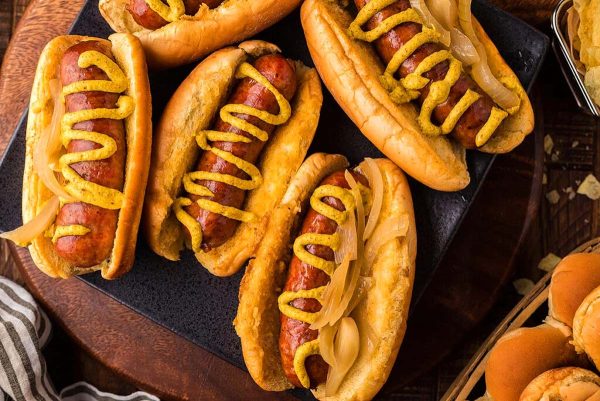 Overhead view of brats in buns and with mustard on them.