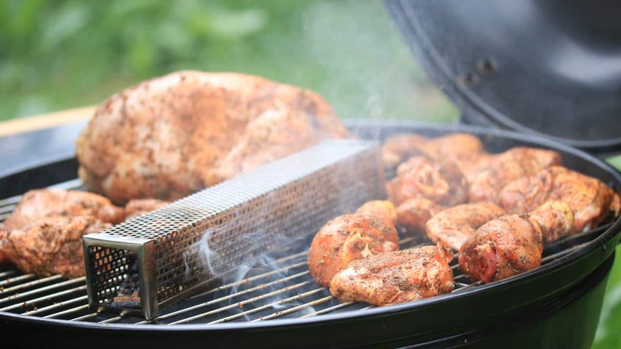 Smoker tube on a barbecue grill next to grilled meats.