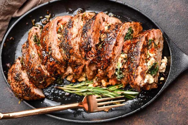 Pork tenderloin on a black plate with a fork.