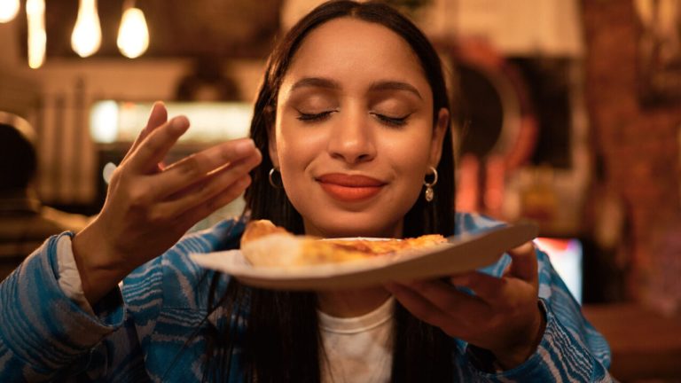 Woman holding up a slice of pizza before eating it.