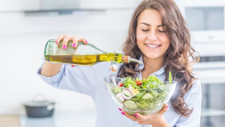 Young woman pouring olive oil into a salad.