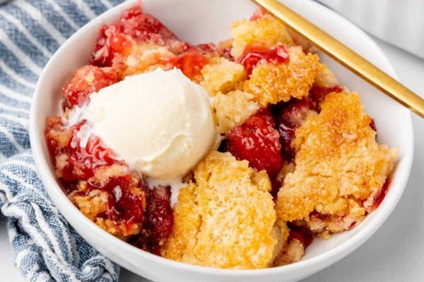 Delicious strawberry cobbler recipe served in a white bowl with a scoop of creamy ice cream.