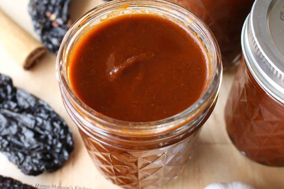 A jar of sauce with a cinnamon stick next to it, perfect for adding a unique twist to your recipes.