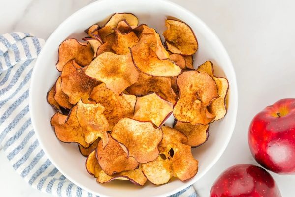 Cheap apple chips in a white bowl next to apples.