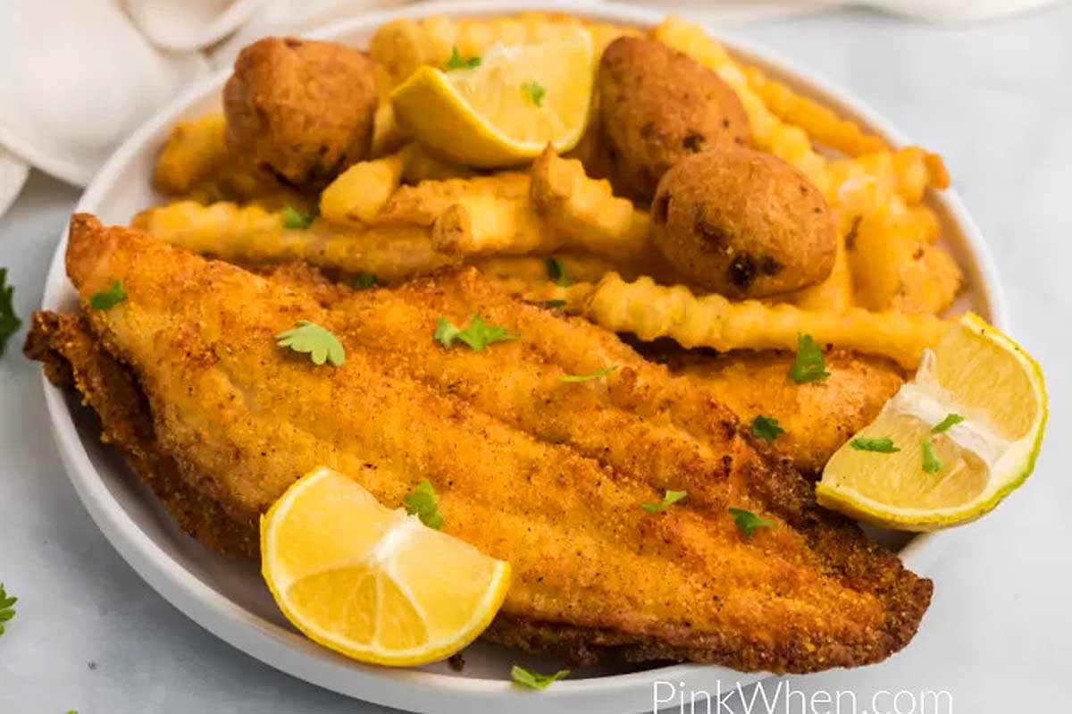Fish fillets with fries and lemon wedges on a white plate.