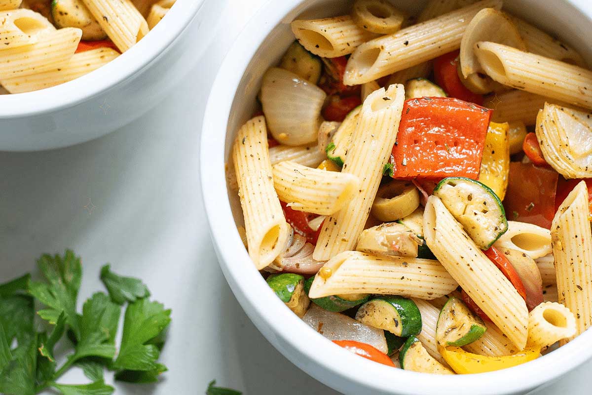 Two bowls of Pasta Salad with vegetables and parsley.