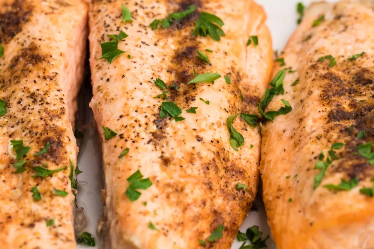 Three salmon fillets with herbs on a white plate, perfect for dinner.