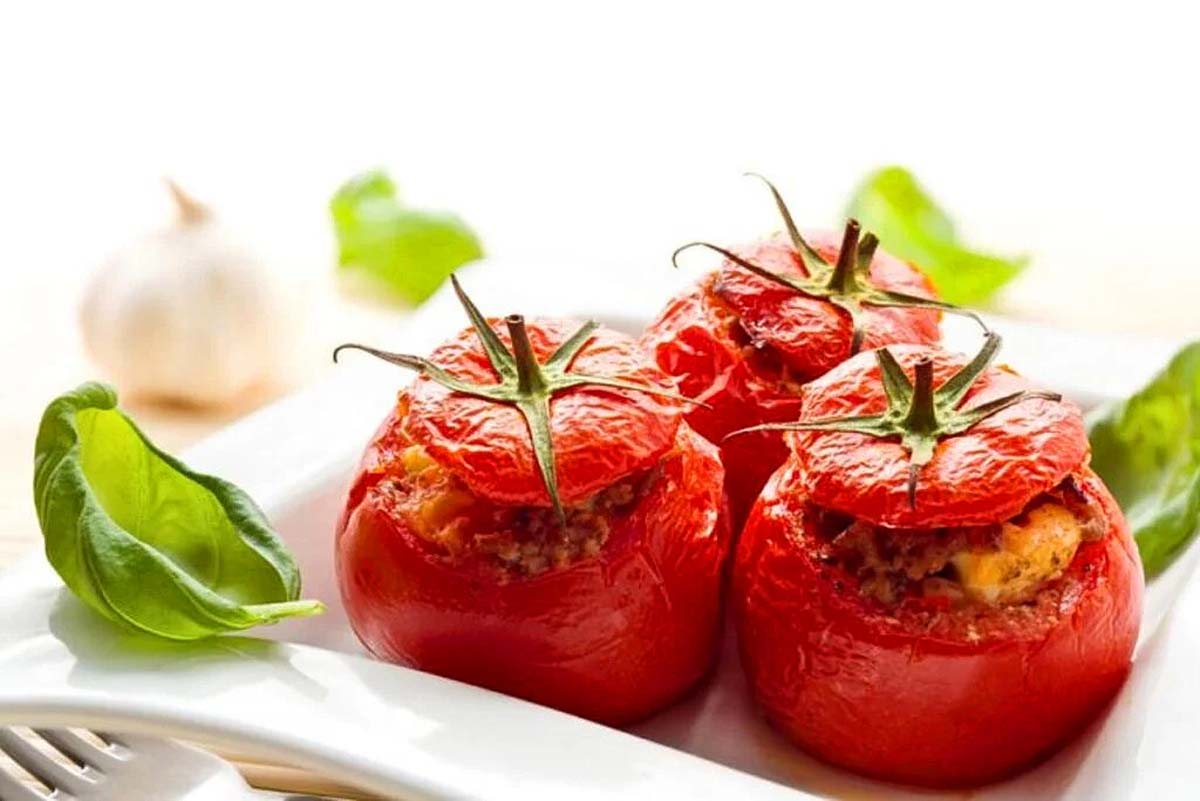 Three stuffed tomatoes on a white plate, perfect for tomato recipes.