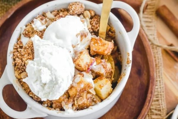Apple crisp in a bowl with whipped cream and cinnamon sticks.