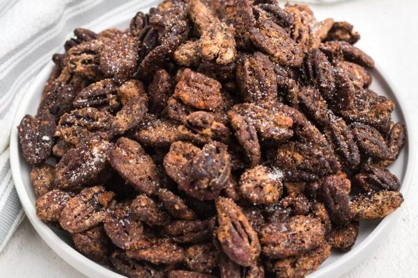 Pecans in a white bowl with a spoon.