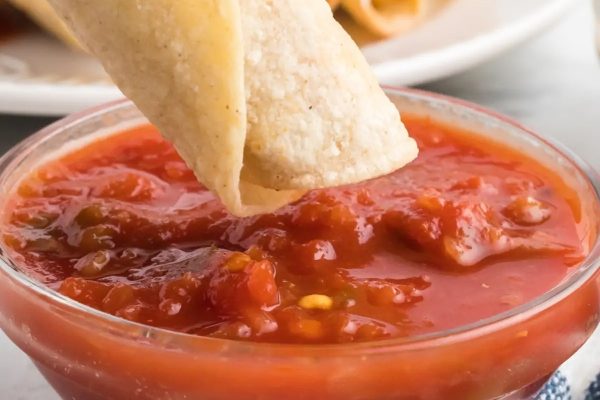 A tortilla being dipped into a bowl of salsa.