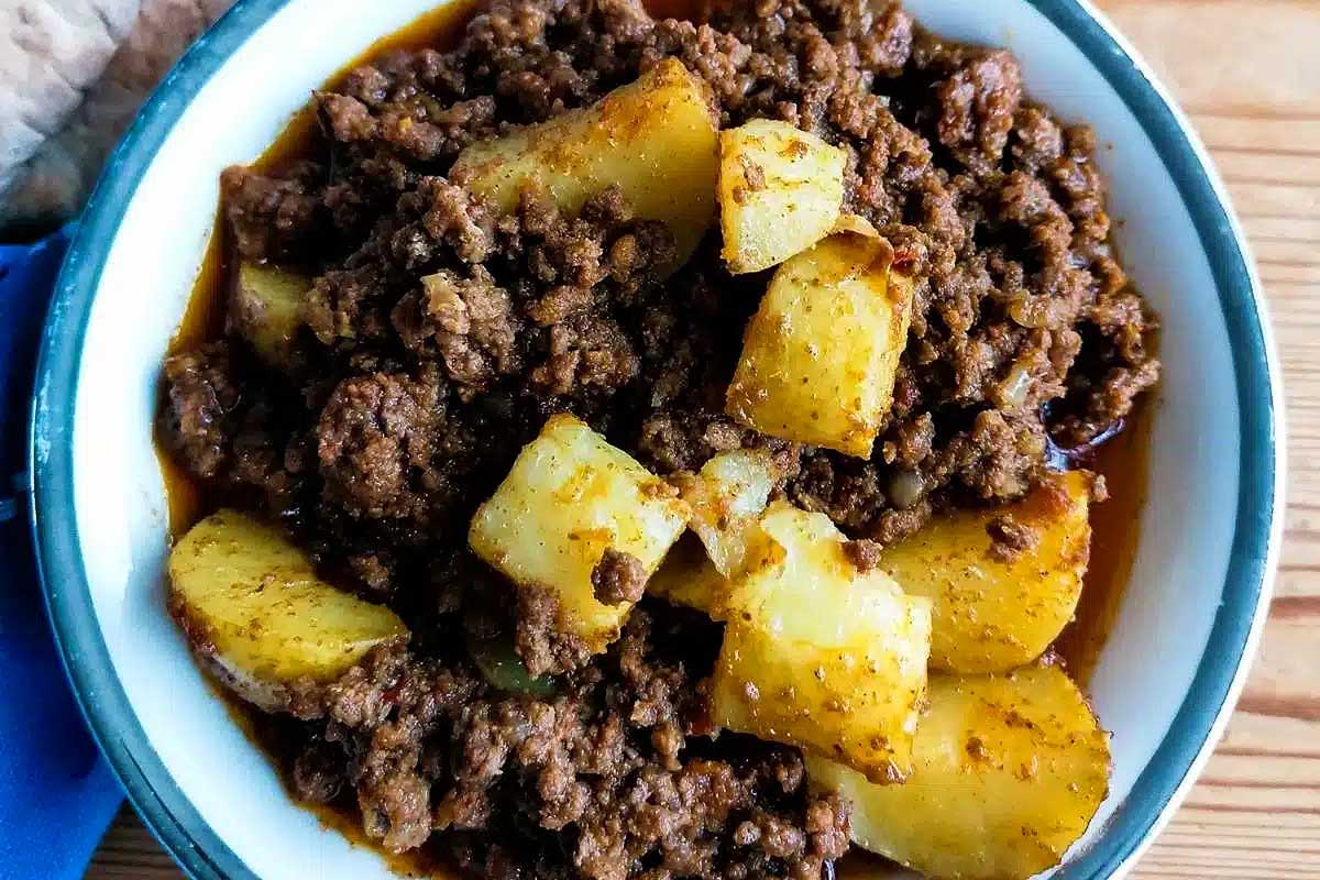 A bowl of beef and potatoes on a wooden table.