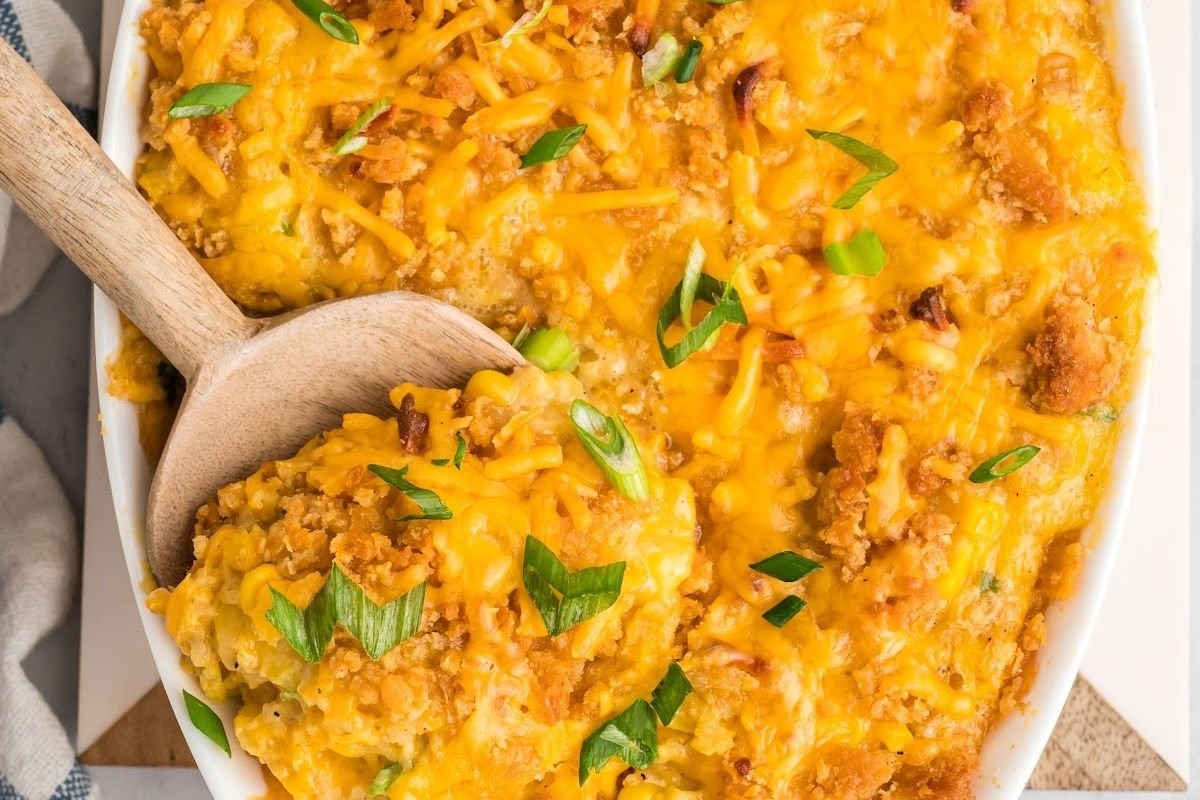 Country-style cheesy corn casserole in a white dish with a wooden spoon, perfect for Thanksgiving recipes.