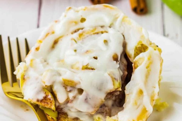 A delectable cinnamon roll with a generous drizzle of icing and accompanied by cinnamon sticks on a plate.