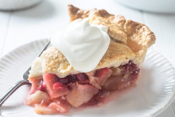 A slice of cranberry pie on a plate with whipped cream.