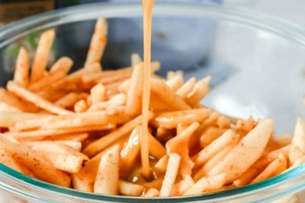 A bowl of french fries being dipped in a sauce.