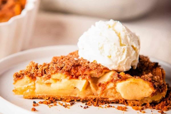 A slice of apple pie with whipped cream on a plate.