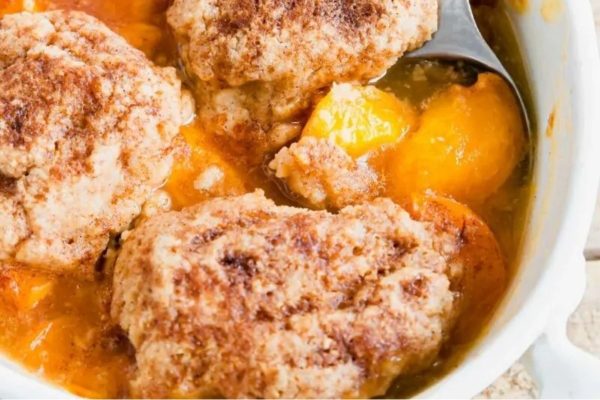 Peach cobbler in a white dish with a spoon.