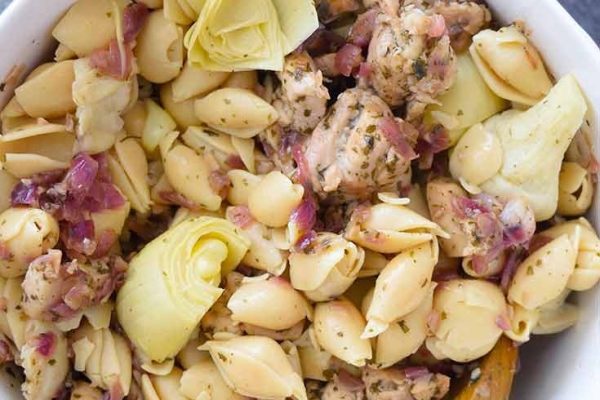 A delicious pasta recipe featuring tender chicken and artichokes served in a white bowl.