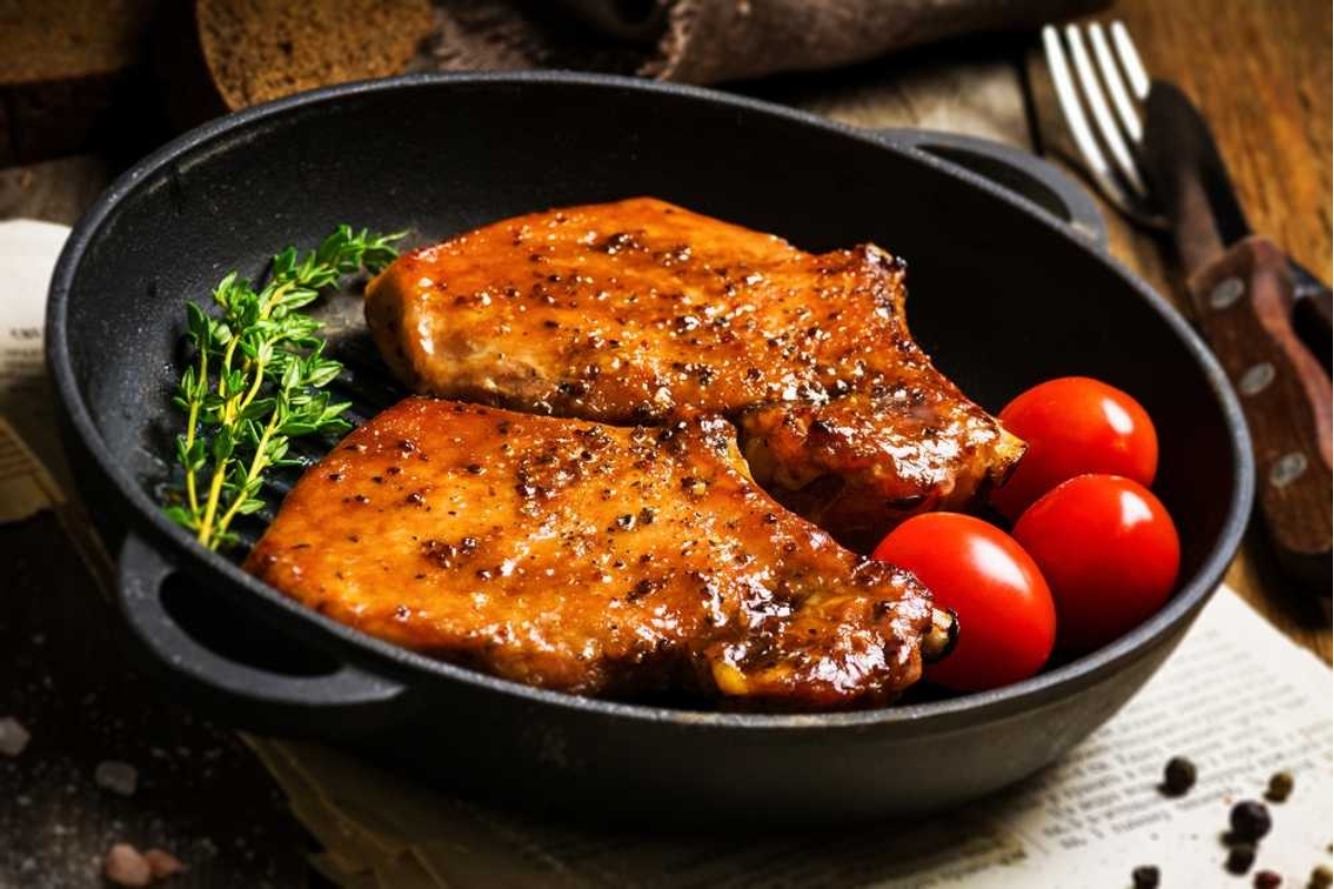 Pork chops in a skillet with tomatoes and herbs.