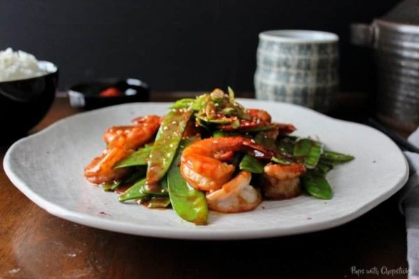 A white plate with shrimp and green peas on it.