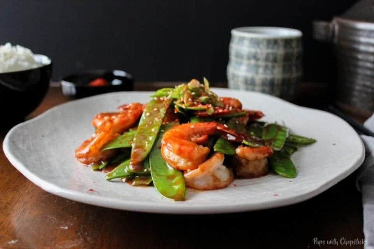 A white plate with shrimp and green peas on it.
