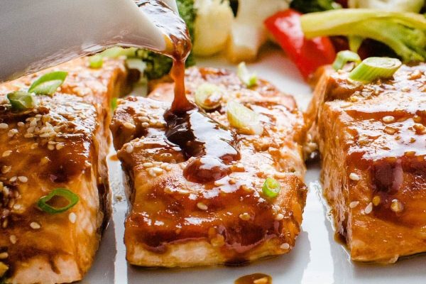 A delectable Asian glazed salmon recipe being gracefully poured onto a plate, offering a delightful seafood experience.