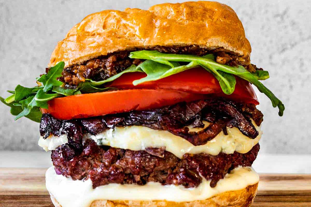 A burger with cheese, tomatoes and lettuce on a wooden cutting board.
