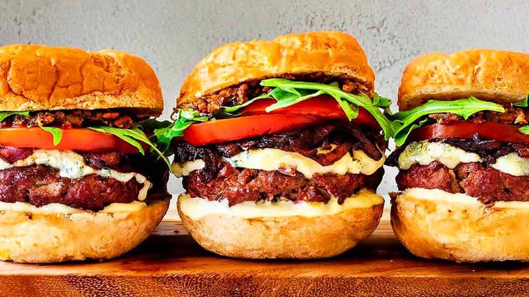 Three burgers on a cutting board.