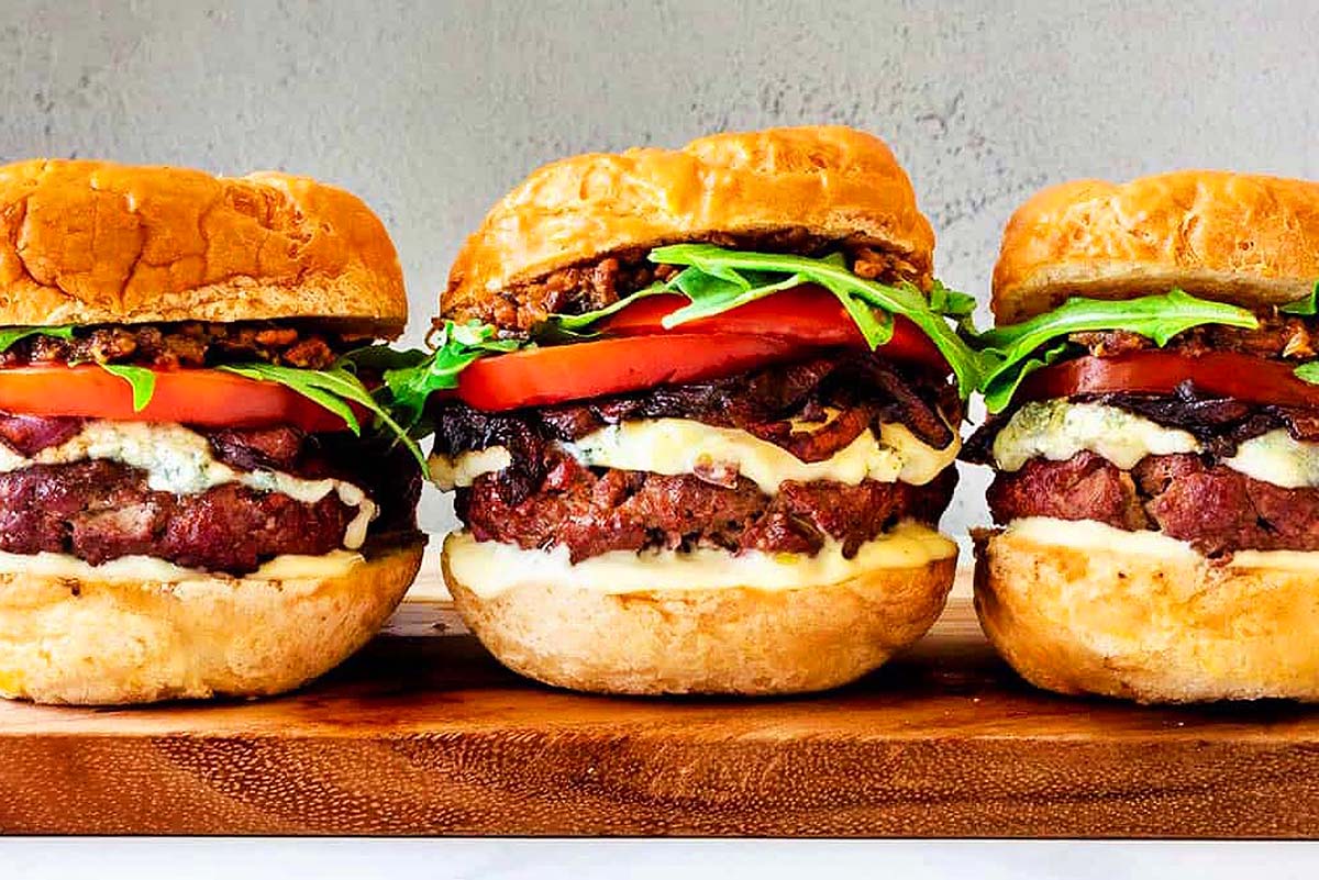Four burgers sitting on a wooden cutting board. This is one of the best burger recipes.