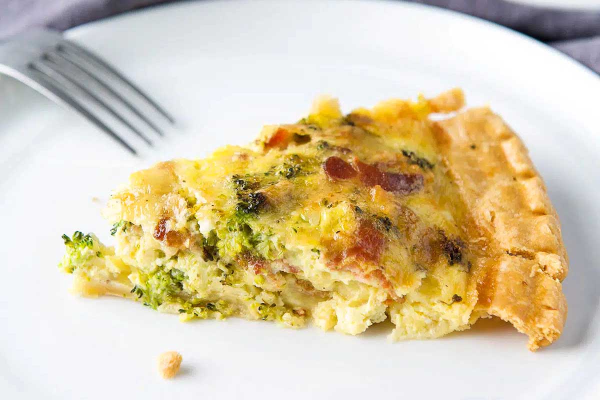 A slice of broccoli quiche on a white plate.