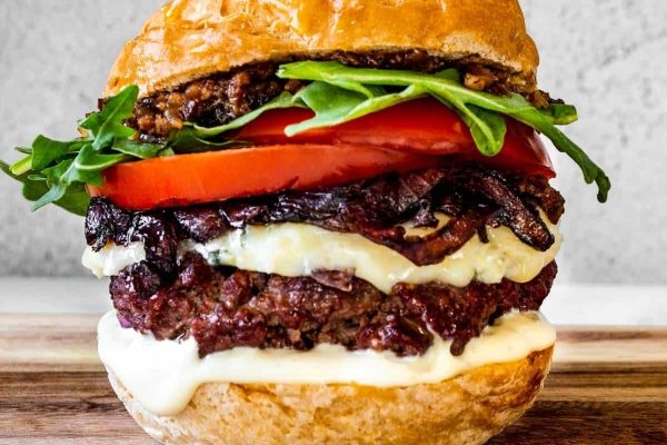 A burger with cheese and tomatoes on a wooden cutting board.