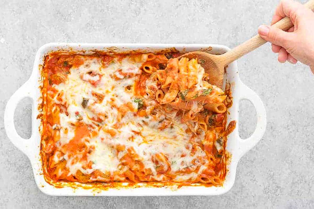 A hand reaching into a casserole dish with a wooden spoon.