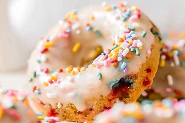 Donuts with sprinkles and icing on a white plate.