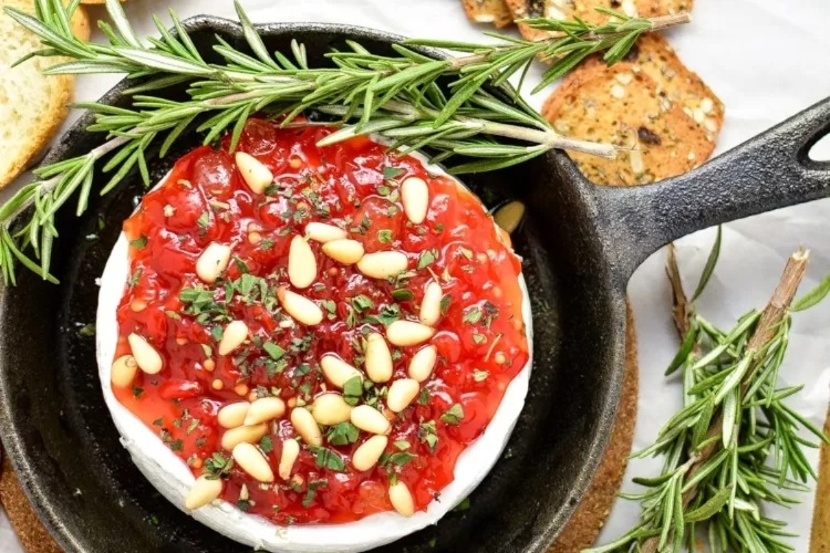 An appetizing bowl of roasted red pepper and goat cheese dip with rosemary sprigs, perfect for Christmas party appetizers.
