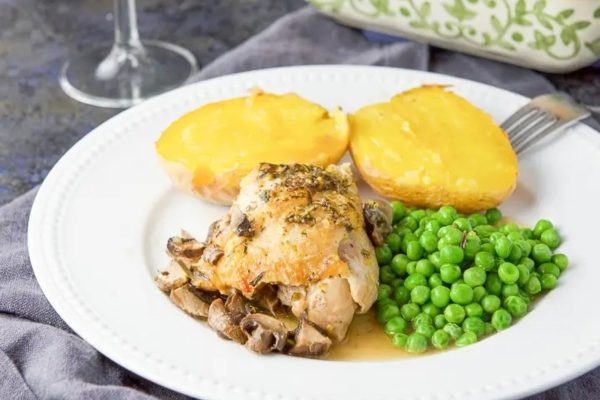 Chicken with mushrooms and peas on a white plate with a glass of wine.