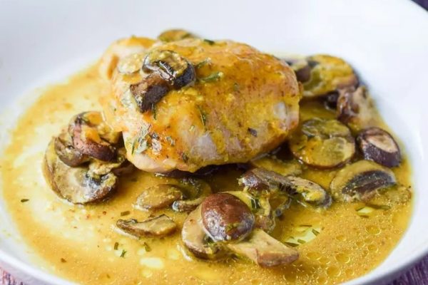 A white plate with chicken and mushrooms in a sauce.