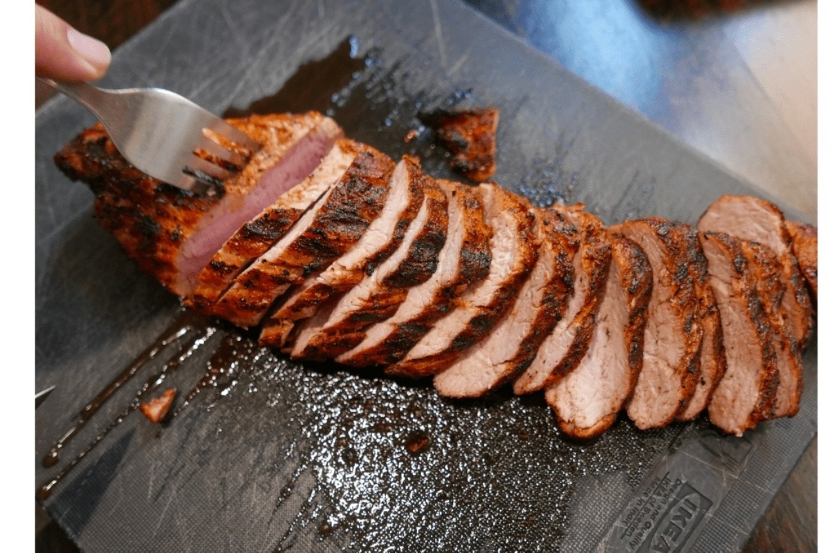 At a dinner party, a person is skillfully slicing a main piece of meat on a cutting board.