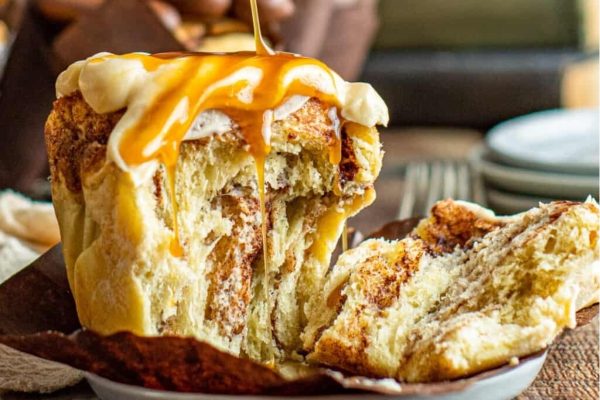 A decadent cinnamon roll is being generously drizzled with a luscious caramel sauce, creating the perfect indulgence for any dessert lover.
