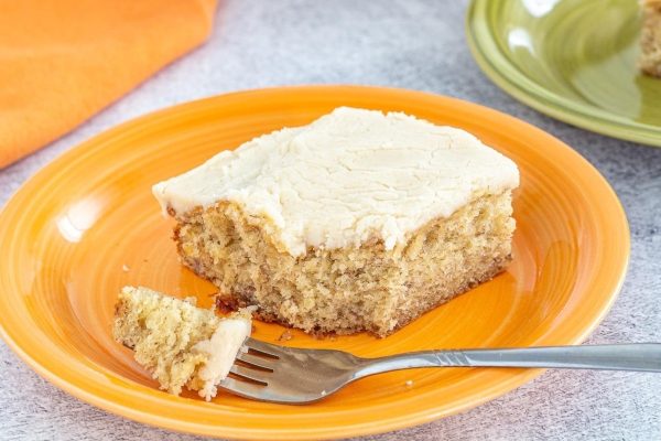 A slice of banana cake on an orange plate with a fork.