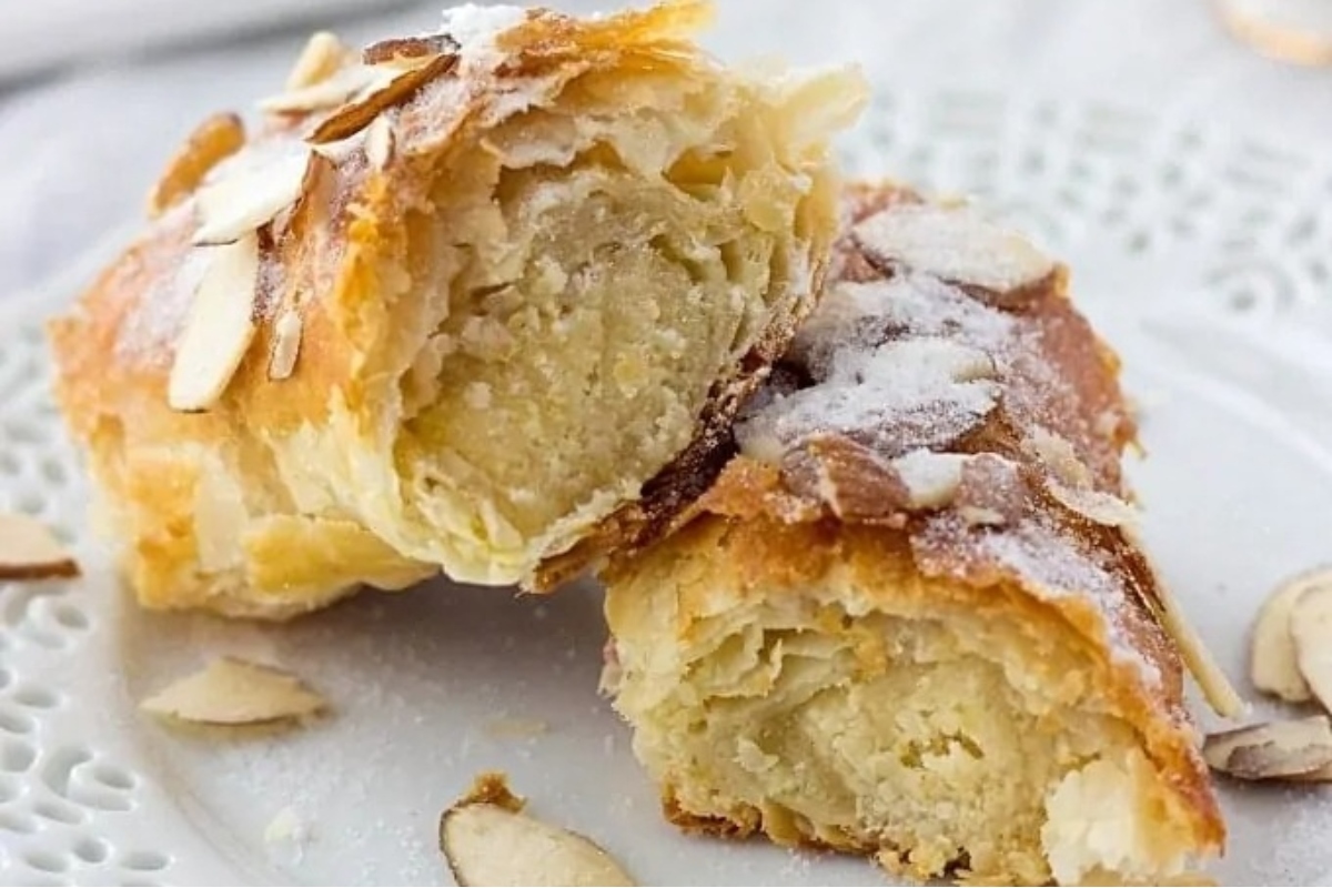 A plate with two mouthwatering puff pastries topped with almonds and a dusting of powdered sugar.