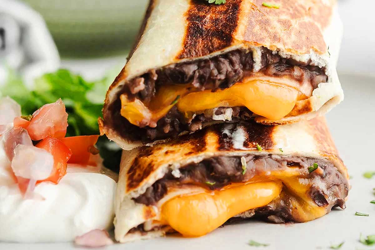 A burrito with cheese and tomatoes on a plate.