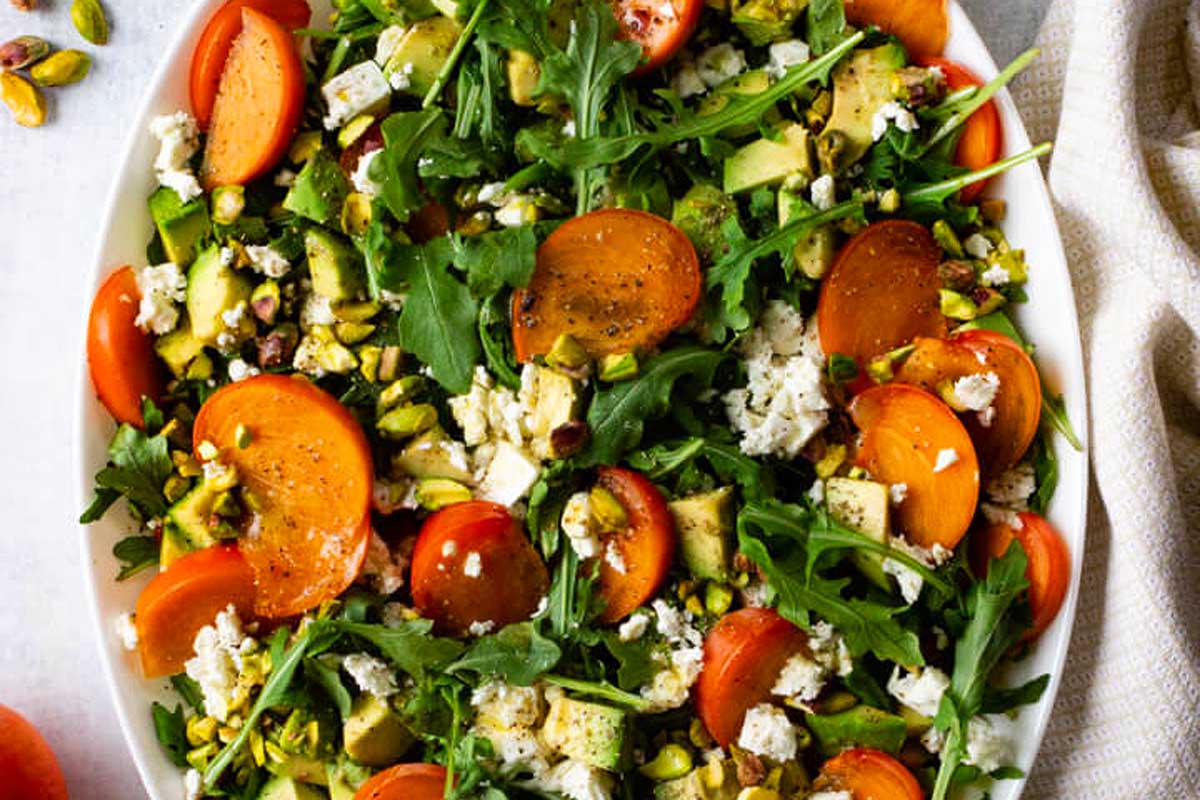 A salad with tomatoes, feta and pistachios on a white plate.