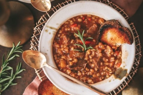 A bowl of stew with bread and rosemary.