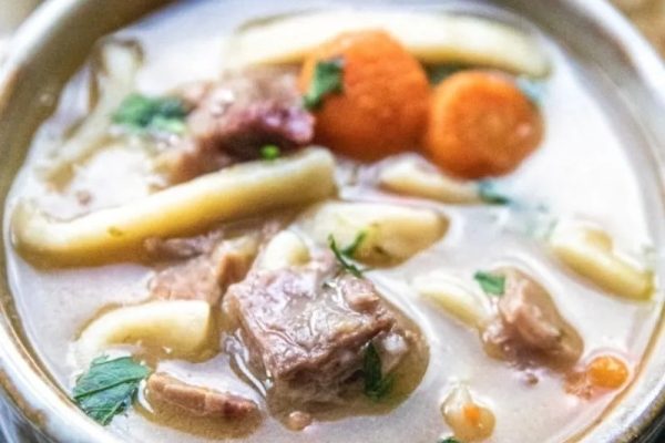 A bowl of beef noodle soup with carrots and noodles.