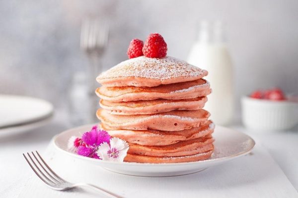A stack of pancakes with raspberries and powdered sugar.
