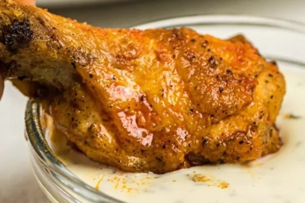 A person is dipping a chicken wing into a bowl of sauce on game day.