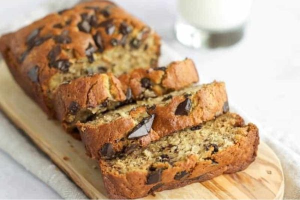 Chocolate chip banana bread on a cutting board with a glass of milk.