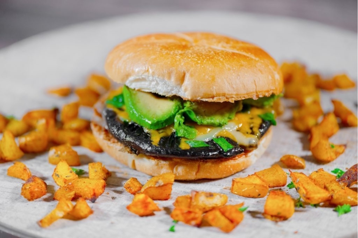 A mushroom burger served on a bun with avocado and potatoes on a plate.